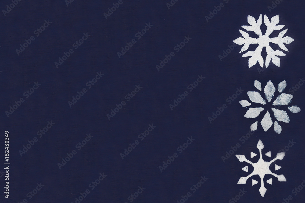A few white snowflakes are painted through a stencil on a dark blue background. Copy space. A few white snowflakes are painted through a stencil on a dark blue background. Copy space.
