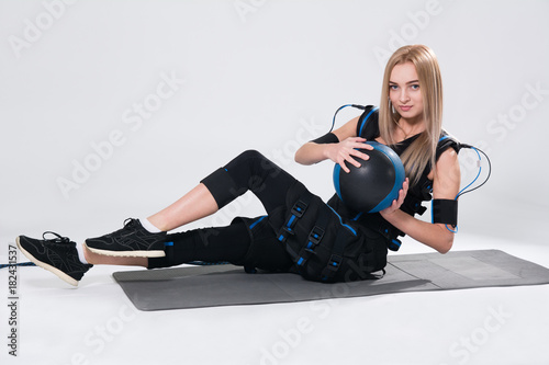 Beautiful blonde in an electric muscular suit to stimulate with a training ball