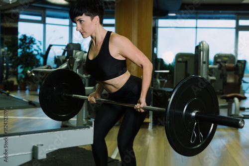Fit young woman lifting barbells looking focused, working out in a gym, doing barbell row