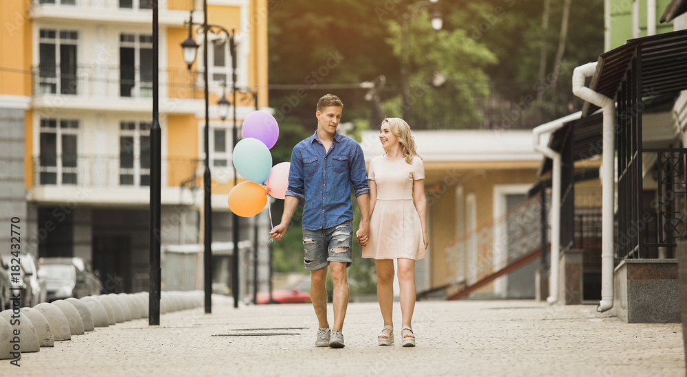 Male with balloons and female strolling down street and talking, romantic date