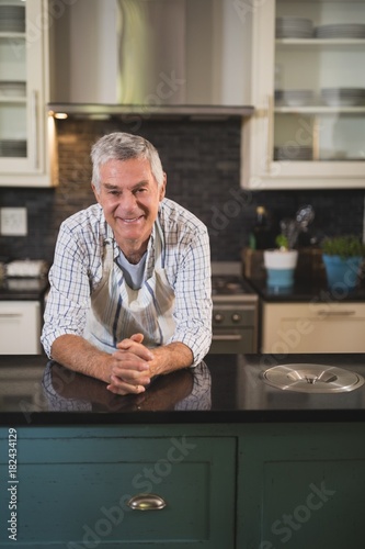 Smiling senior man wearing apron in kitchen at home