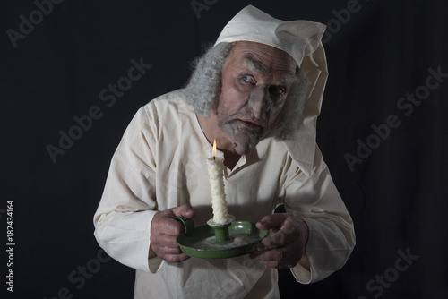 Mature man in old fashioned Victorian night shirt holding a candle 