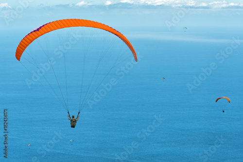 colored paragliders above blue ocean on cloudy sky background