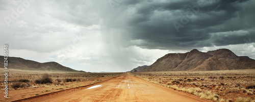 Red sandy road with heavy rainfall and thunderstorm in the distance, Tiras Mountain Range, Namib Naukluft National Park, Namibia, Africa