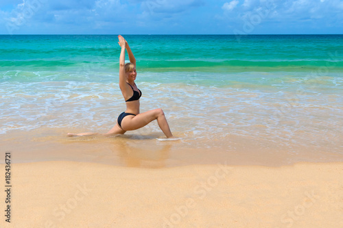 Young woman doing yoga on the beach in hero pose.