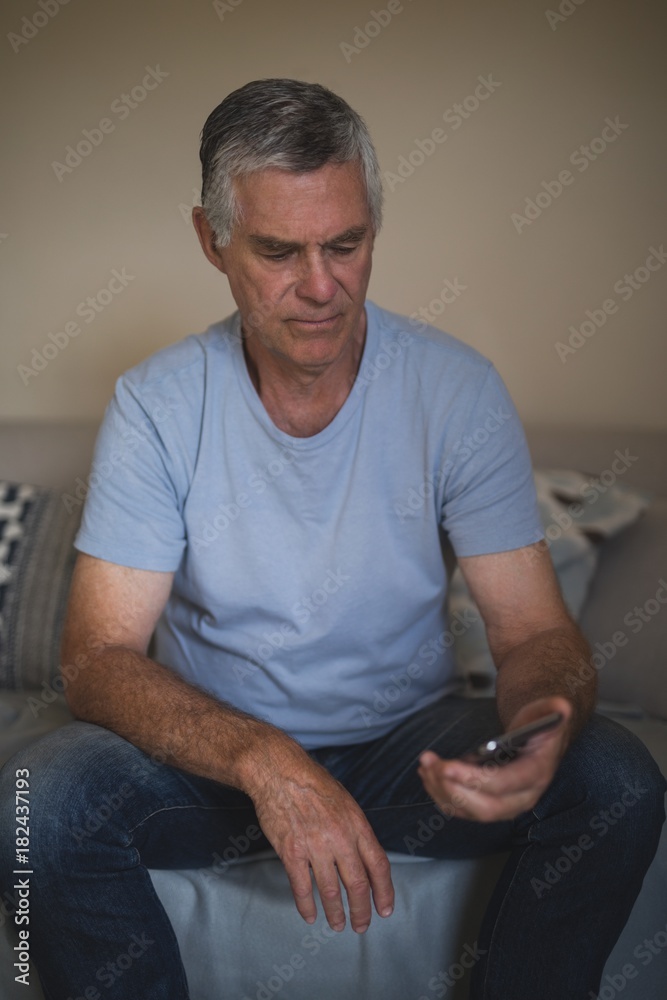 Upset senior man holding mobile phone while sitting on sofa Upset senior man holding mobile phone while sitting on sofa