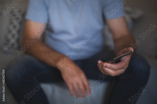 Mid section of man holding mobile phone while sitting on sofa