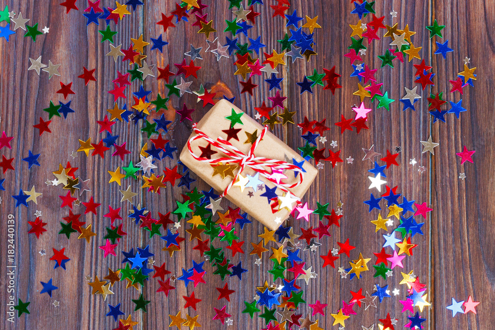 Gift box with star. Creative concept with festive decor on black background. Confetti stars, red, yellow with gift box. Explosion of confetti
