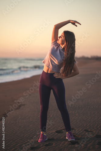 Beautiful young woman doing exercise on the sandy beach, healthy relaxation.