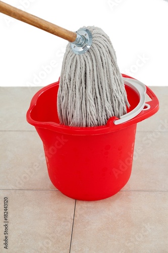 Mop in red bucket on tile floor