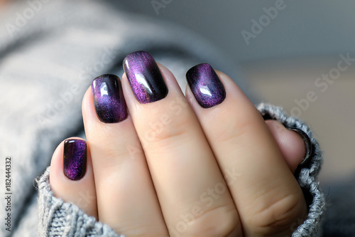 Beautiful nail polish in hand, purple nail art manicure, gray background