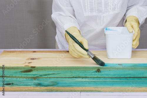 Una persona da color a una madera con una brocha y tinte azul