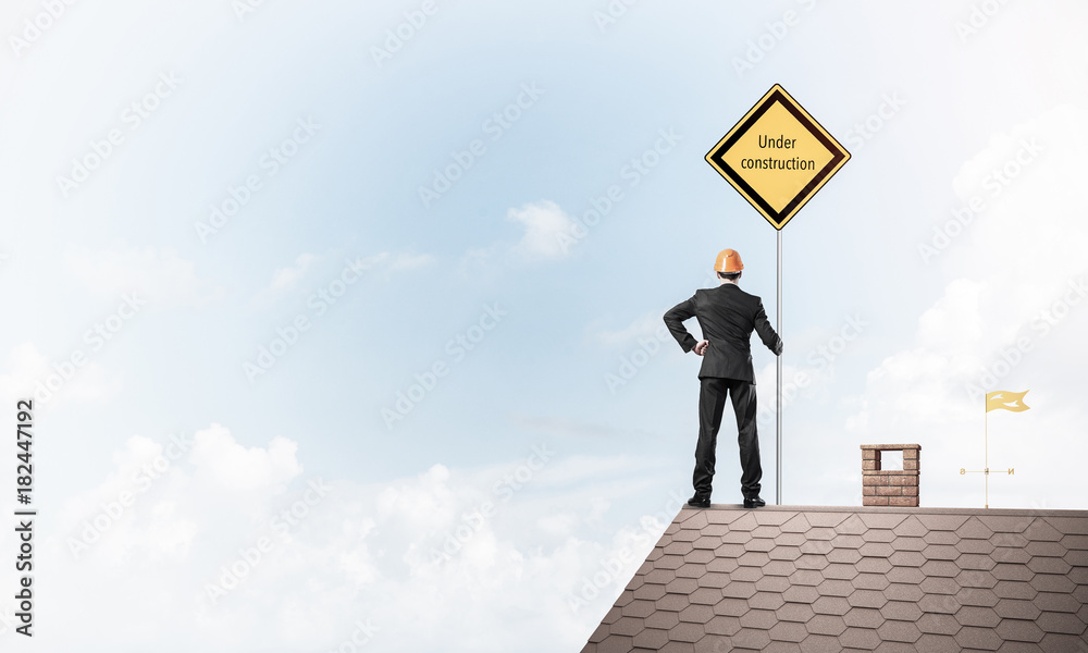 Young businessman on house brick roof holding yellow signboard. Young businessman on house brick roof holding yellow signboard.