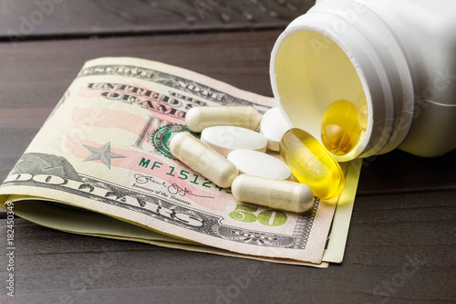 Yellow capsules of omega-3 in bottle, white capsules of glucosamine, white pills of calcium and dollars banknote at wooden table photo