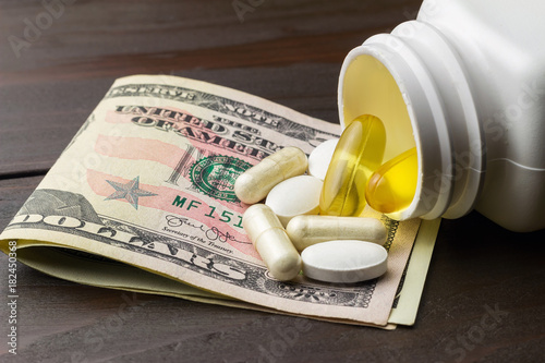 Yellow capsules of omega-3 in bottle, white capsules of glucosamine, white pills of calcium and dollars banknote at wooden table photo