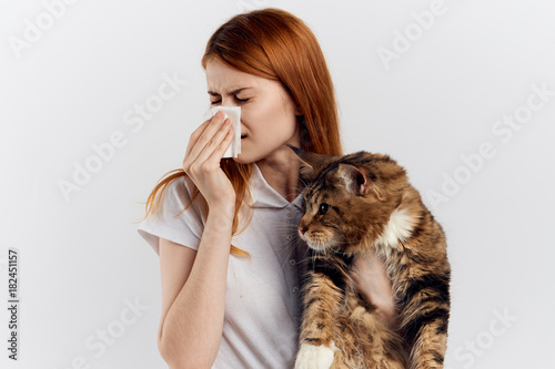 1993244 Young beautiful woman holding a cat on a light background, allergic to pets