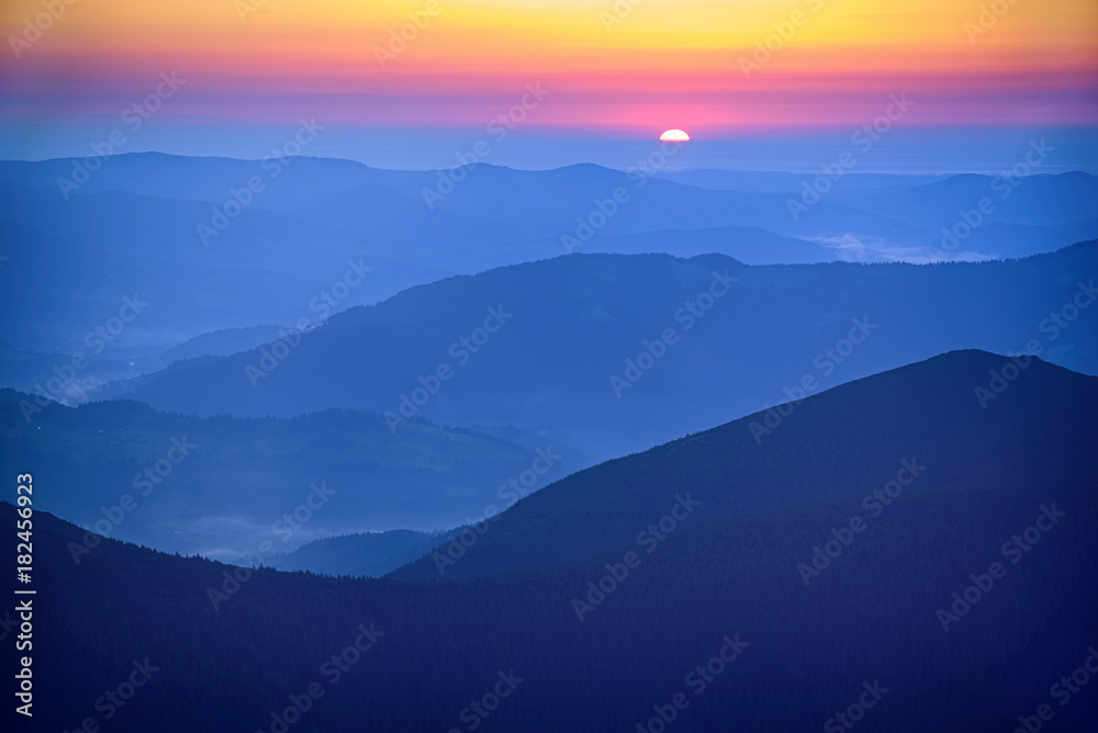 Amazing mountain landscape with colorful vivid sunrise on the bright sky over blue hills, natural outdoor travel background