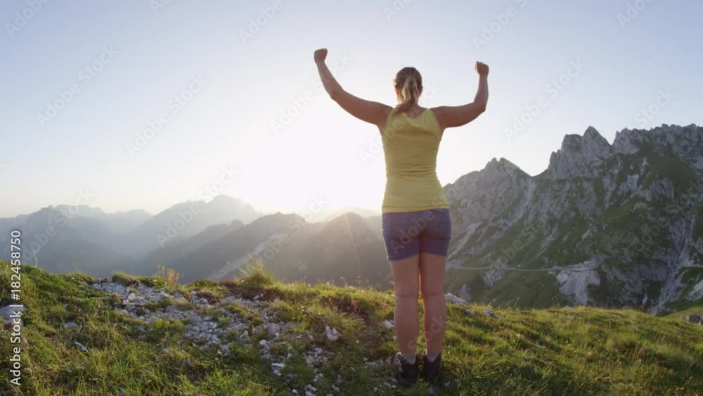 SLOW MOTION Happy woman raising her arms victoriously on rocky mountaintop at golden sunset. Hiking girl outstretching arms when reaching top of mountain at sunrise. Young trekker achieving daily goal SLOW MOTION Happy woman raising her arms victoriously on rocky mountaintop at golden sunset. Hiking girl outstretching arms when reaching top of mountain at sunrise. Young trekker achieving daily goal