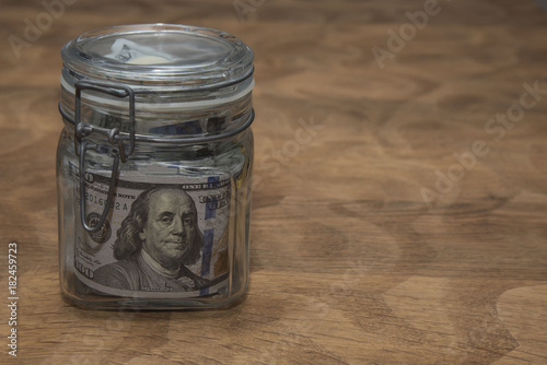 A stack of American hundred dollar bills lying in a glass jar.