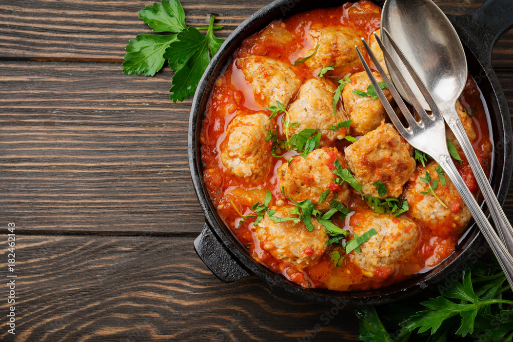 Meatballs in tomato sauce garlic and parsley in an iron frying pan on a dark brown wooden background. Selective focus. Top view. Copy space. Meatballs in tomato sauce garlic and parsley in an iron frying pan on a dark brown wooden background. Selective focus. Top view. Copy space.