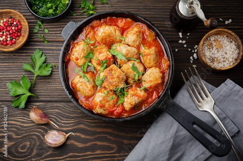 Meatballs in tomato sauce garlic and parsley in an iron frying pan on a dark brown wooden background. Selective focus. Top view. Copy space. photo