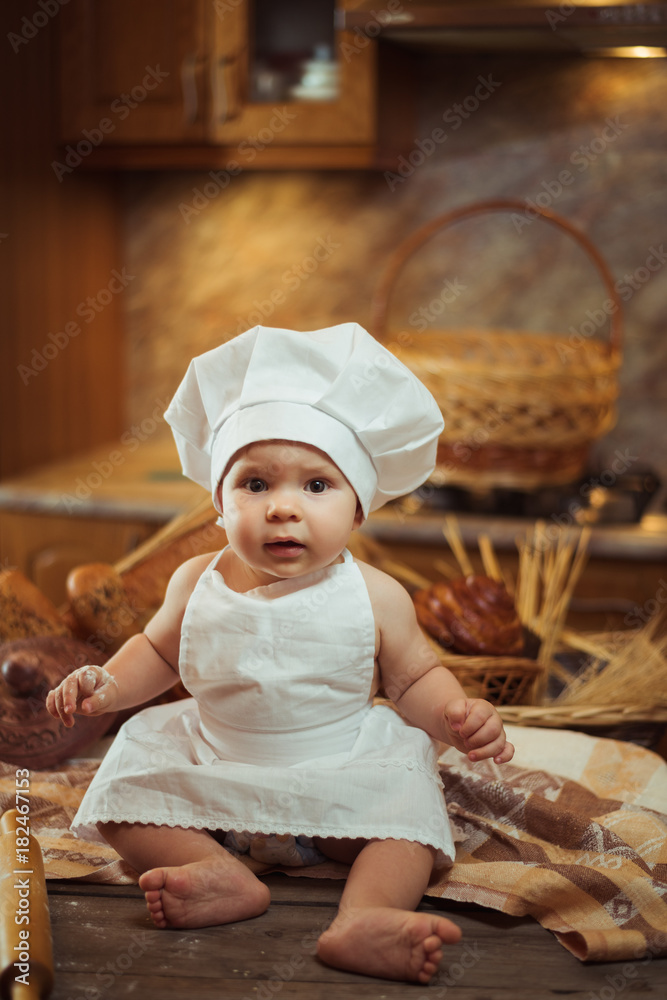 Happy little child in the cook costume at the kitchen sitting on the table  among baskets with tasty rolls, buns and bread. Copy space Stock Photo |  Adobe Stock