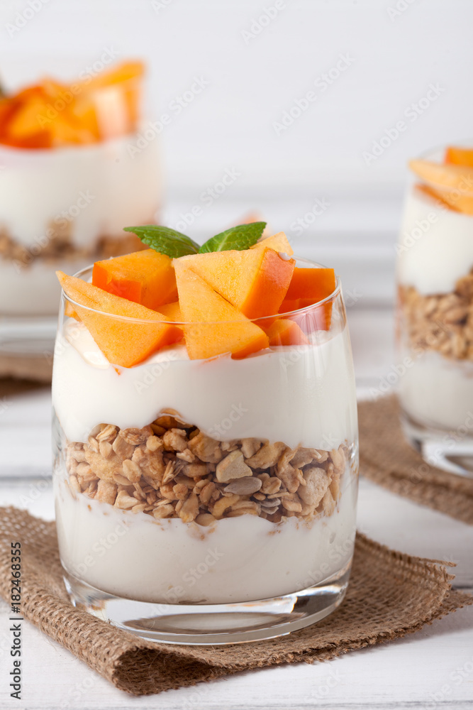 Persimmon creamy trifle in beautiful glasses, fresh ripe fruit slices on white wooden background. Healthy vegetarian food. Delicious dessert. Close up photography. Selective focus. Persimmon creamy trifle in beautiful glasses, fresh ripe fruit slices on white wooden background. Healthy vegetarian food. Delicious dessert. Close up photography. Selective focus.