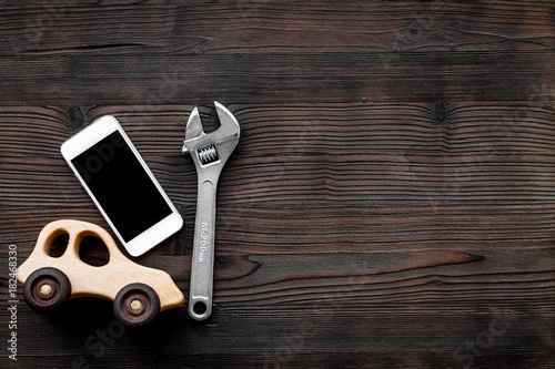 Choose car service. Wrench near car toys and cell phone on dark wooden background top view copyspace