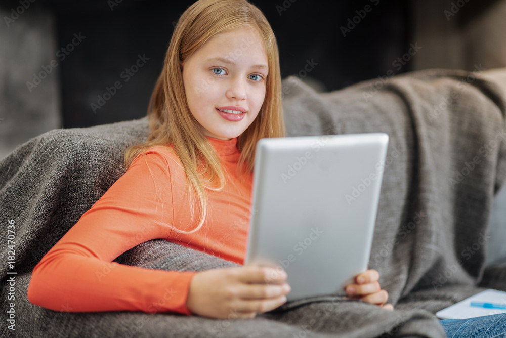 Modern generation. Pretty pleasant young girl sitting at home and using her tablet while entertaining herself Modern generation. Pretty pleasant young girl sitting at home and using her tablet while entertaining herself