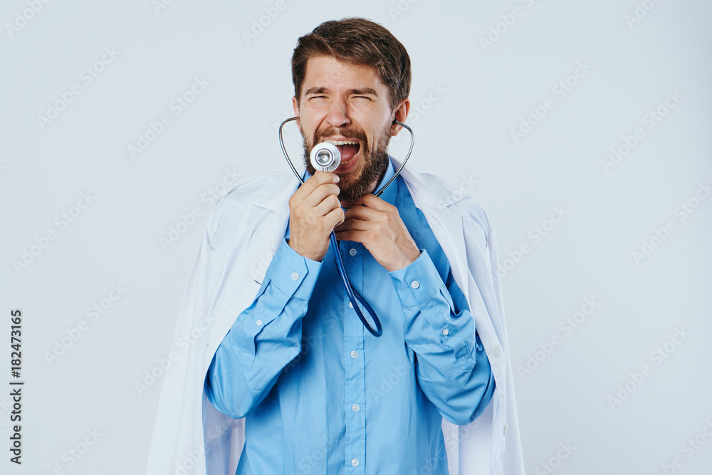 Man with a beard on a light background in a medical dressing gown holds a stethoscope, doctor, medicine Man with a beard on a light background in a medical dressing gown holds a stethoscope, doctor, medicine