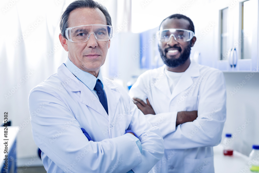 Professional team. Delighted nice positive scientists standing together and looking at you while working in team in the lab Professional team. Delighted nice positive scientists standing together and looking at you while working in team in the lab