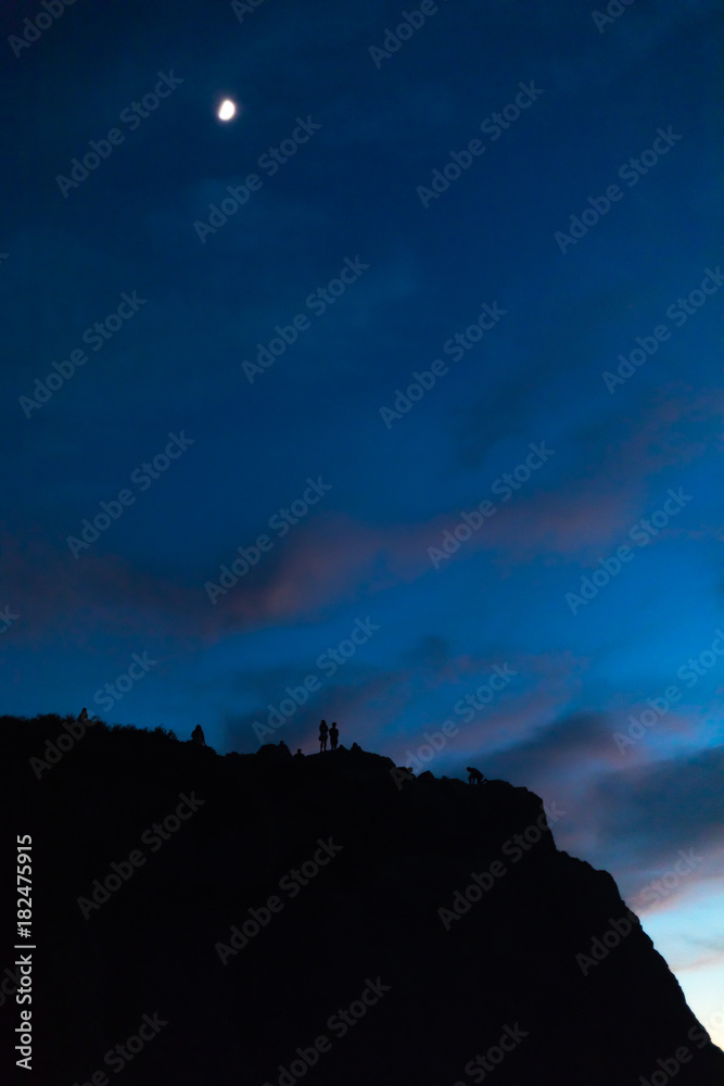 Vertical Observing the sunset and moon at twilight on Point Dume, Malibu in silhouette with colorful pink clouds and deep blue sky