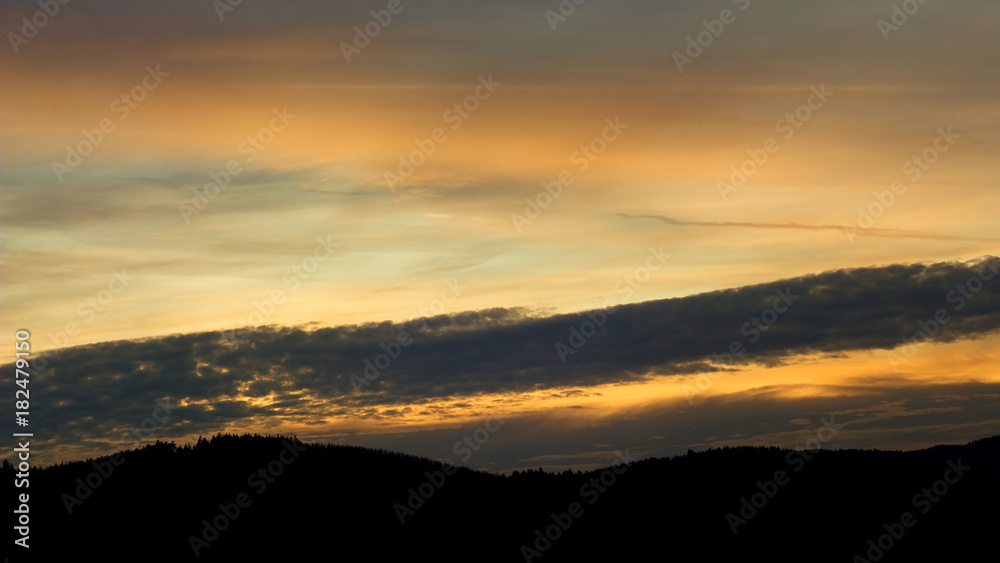 Landscape with forest and silhouettes of trees at sunset between clouds