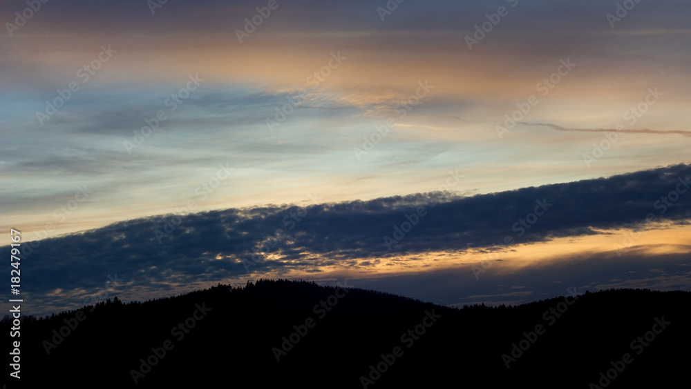 Landscape with forest and silhouettes of trees at sunset between clouds