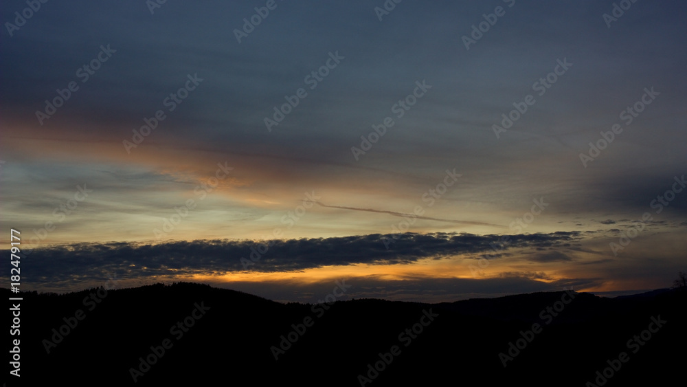 Landscape with forest and silhouettes of trees at sunset between clouds