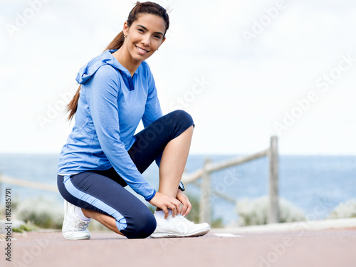 Woman runner tying shoelace at the seaside