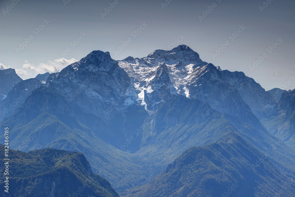 Snow covered Triglav and Rjavina peaks from north with pine forests in deep glacial Vrata, Kot and Sava valleys in sunny autumn morning with blue sky, Triglav National Park Julian Alps Slovenia Europe