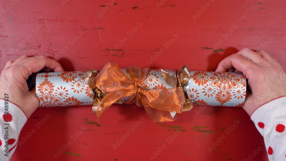 Festive surprise concept, opening a Christmas cracker bon bon with gold glitter stars on rustic red wood table