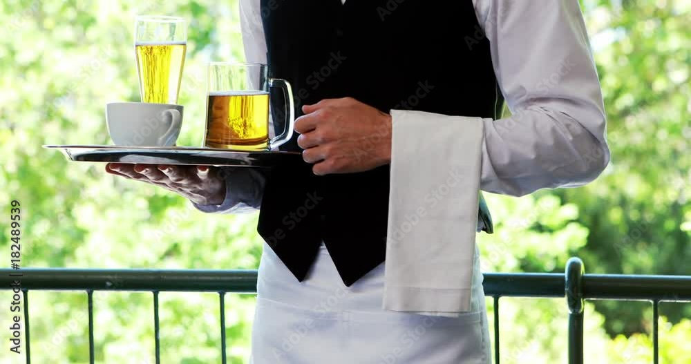 Male waiter holding tray with coffee cup and beer mug in restaurant 