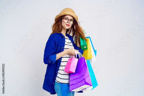 Beautiful woman in a hat and wearing glasses on a light background holds many packages, purchases, a shopaholic