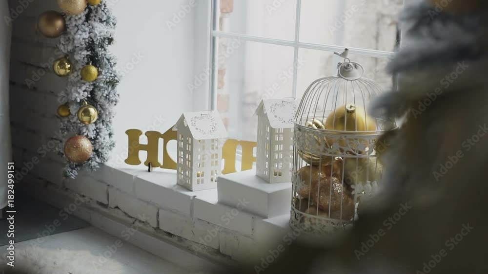 New-year decorative decorations were decorated on the window sill of a large window. New year's Christmas tree is decorated with golden toys near the window New-year decorative decorations were decorated on the window sill of a large window. New year's Christmas tree is decorated with golden toys near the window