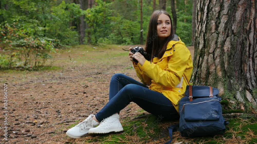 Young amazing woman sitting at the tree and taking photos of the nature on the vintage camera in the green forest. Outdoors Young amazing woman sitting at the tree and taking photos of the nature on the vintage camera in the green forest. Outdoors