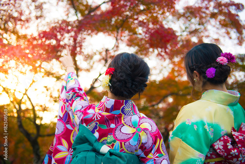  Two Japanese women in Kimono dressing is smiling and enjoy sightseeing maple trees during autumn inside Nara park in Nara-shi, Japan.