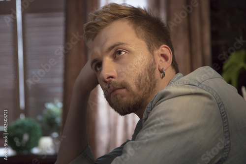 Young man with beard with beautiful hairstyle sitting by window