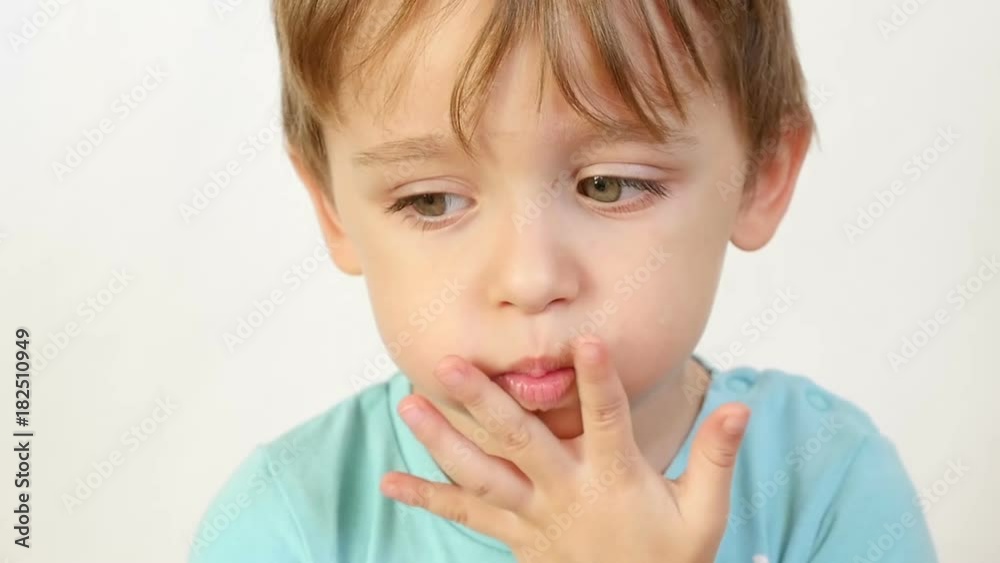 A close-up of a child with an insult, puffed up lips. The child is thoughtful, does not want to hear anybody, keeps fingers at the mouth A close-up of a child with an insult, puffed up lips. The child is thoughtful, does not want to hear anybody, keeps fingers at the mouth