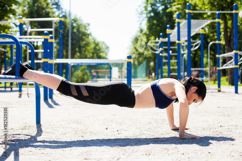 Young sportive girl in a bright blue sport bra and black leggings doing push ups on the sport playground. Photo of an athlete girl with a beautiful sports body