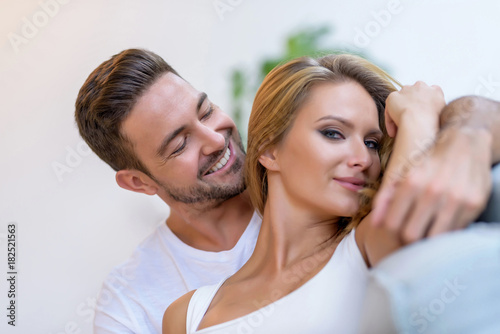 A beautiful young woman lying on the sofa with boyfriend hugging her from behind.