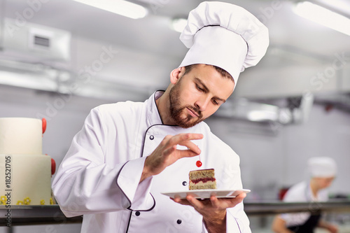 The confectioner is preparing a cake in the kitchen of the pastry shop. photo