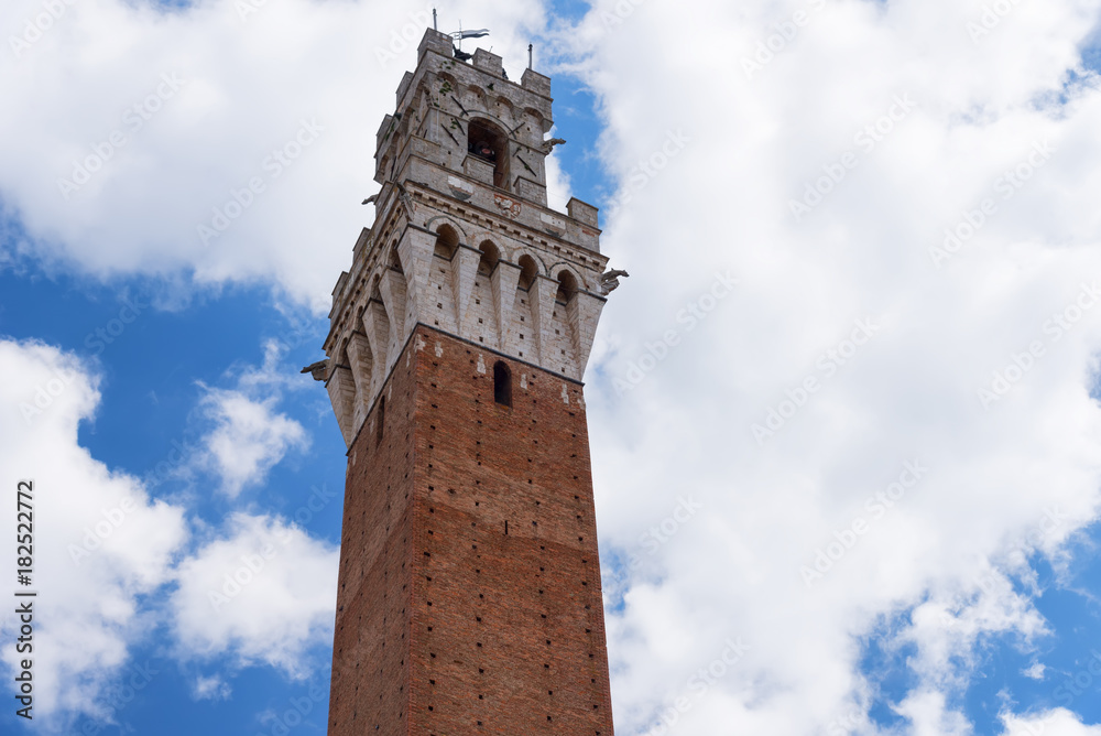Detail of the Torre del Mangia 87 m. (Tower of Mangia) on blue sky with clouds. Siena, Italy
