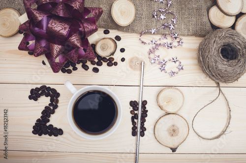 2018 inscription of coffee beans, coffee mug and wooden slices, a gift box with a dark purple bow on light wooden background, top view